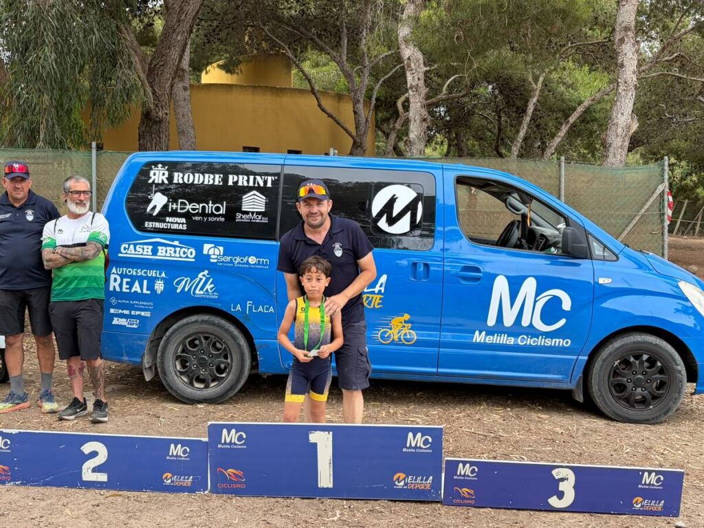 Cuatro personas junto a un vehículo azul en un evento ciclista