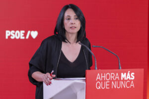 Mujer hablando en un evento del PSOE con fondo rojo