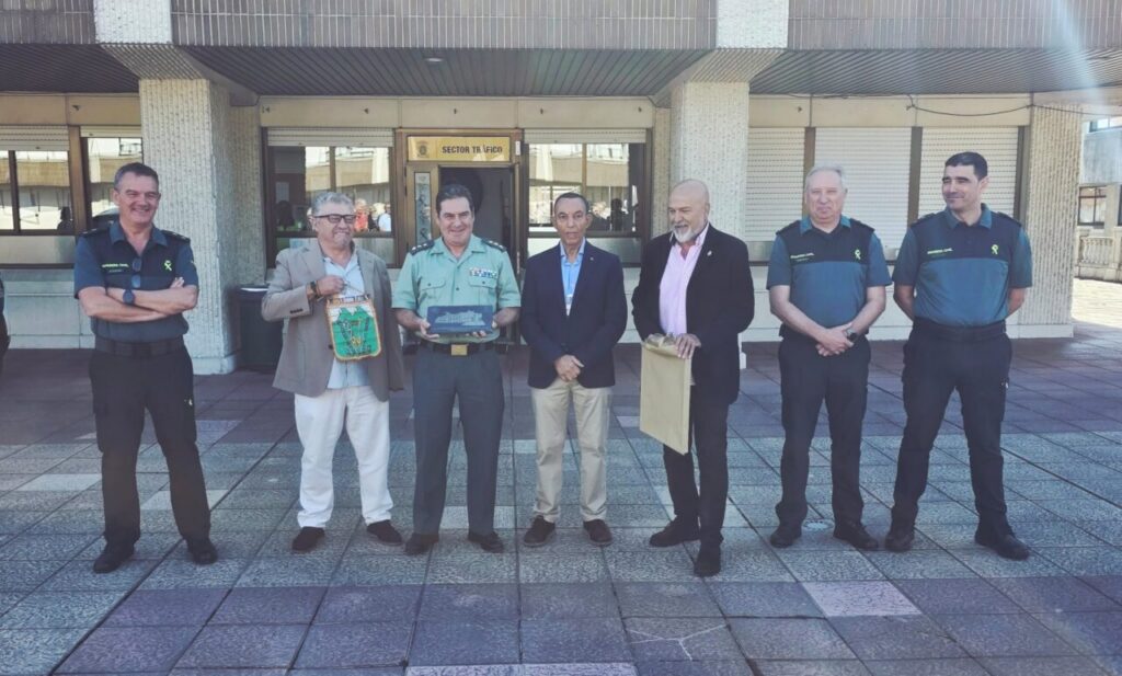 Group of seven men standing in front of a building, some in uniforms, posing for a photo with gifts/bags in their hands.”](#)