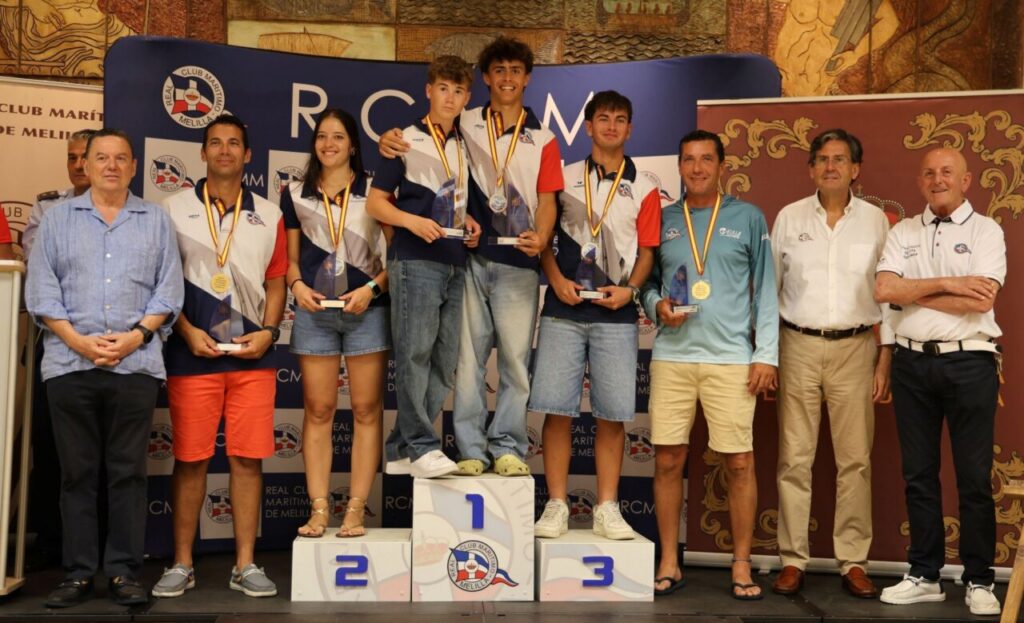 Group of young athletes on a winners' podium with medals, flanked by officials at an award ceremony.