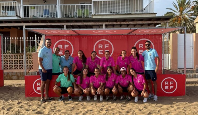 Equipo de fútbol femenino posando en la playa con camisetas de colores