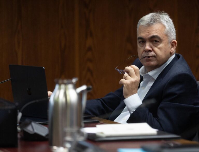 Santos Cerdán en una reunión, sosteniendo gafas, con laptop frente a él.