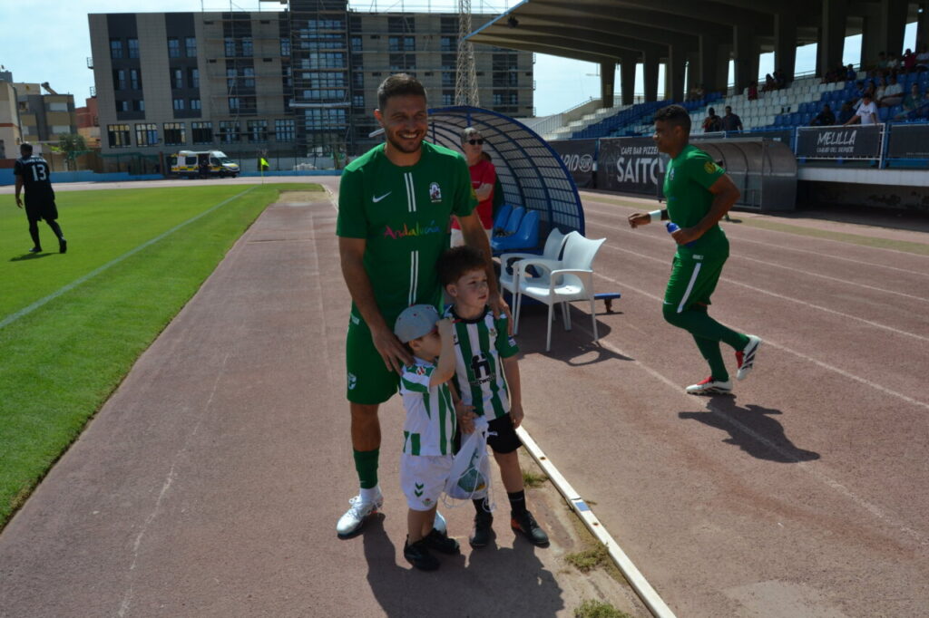Jugador de fútbol con dos niños en el estadio durante un partido amistoso.