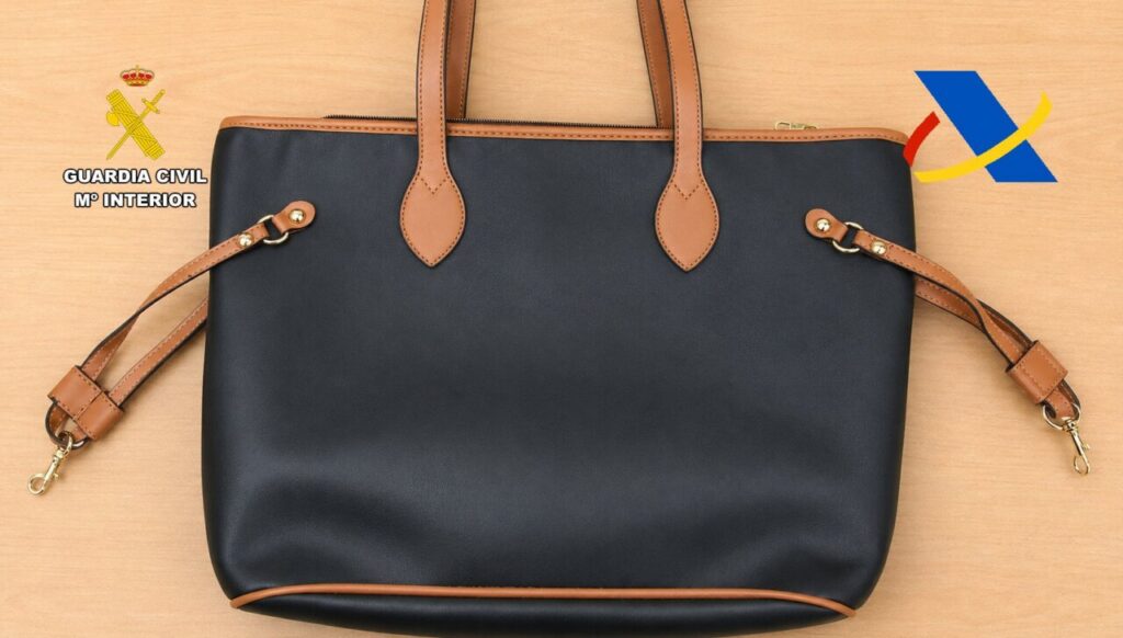 Bolso de mano negro con detalles en marrón sobre una superficie clara