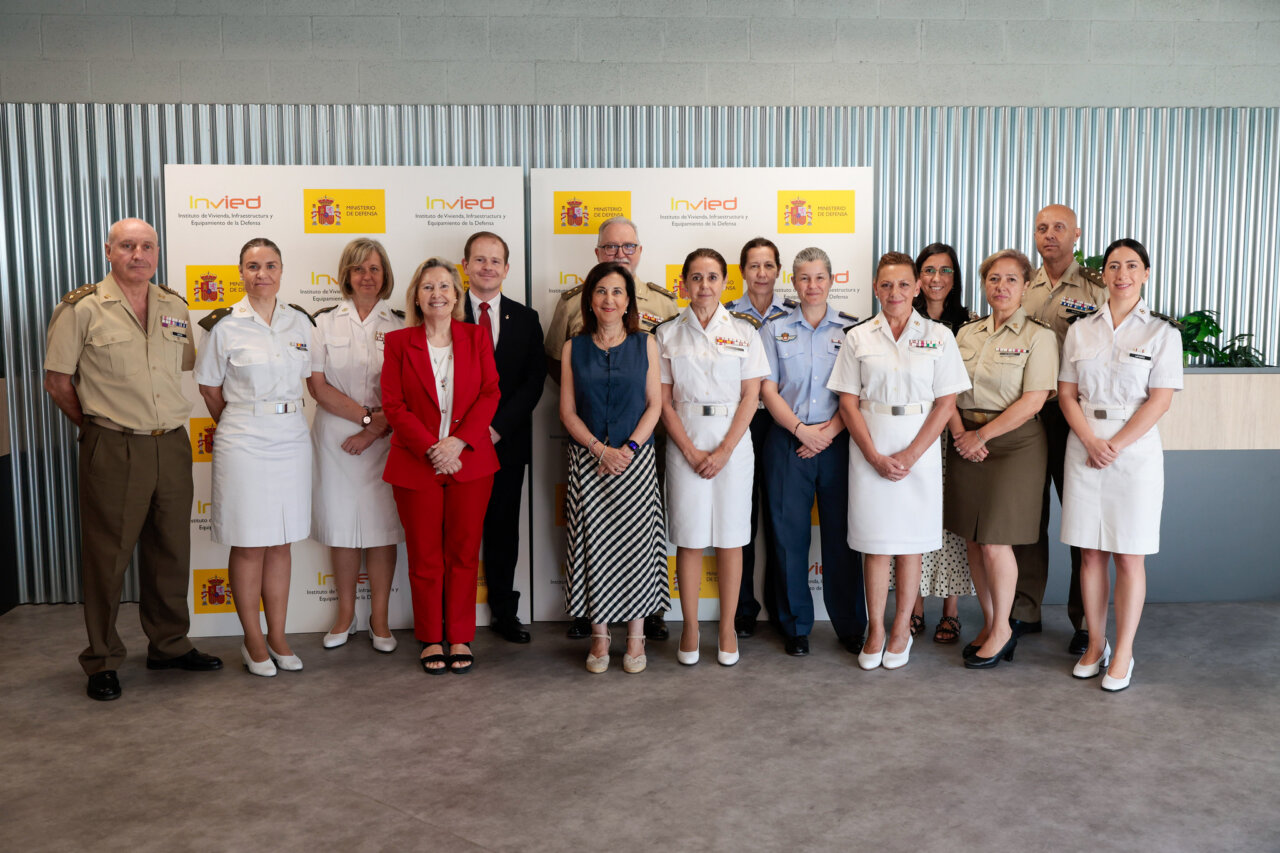 Group of military officers and civilian staff posing for a formal photo in front of a Ministry of Defense backdrop with yellow logos.