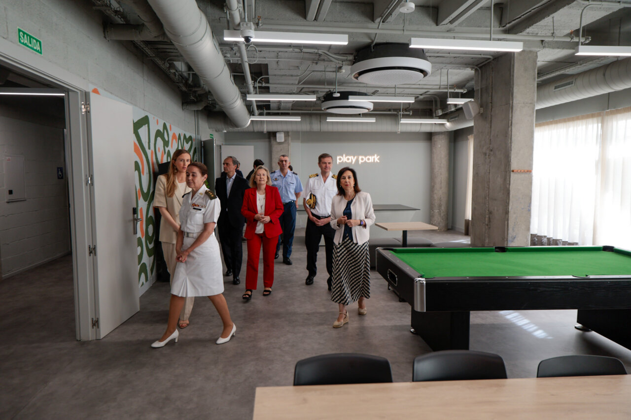 Group of officials and professionals walking through a modern industrial-style recreation space with a green pool table and 'play park' sign in the background.