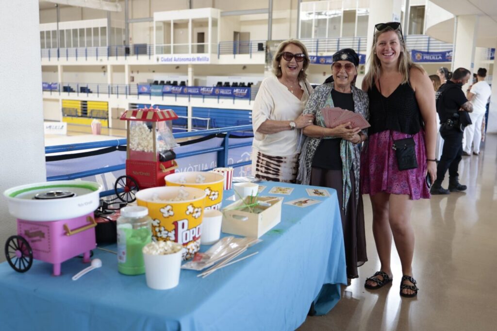 Three women pose together by a snack table with a popcorn machine and cups at an indoor event venue.