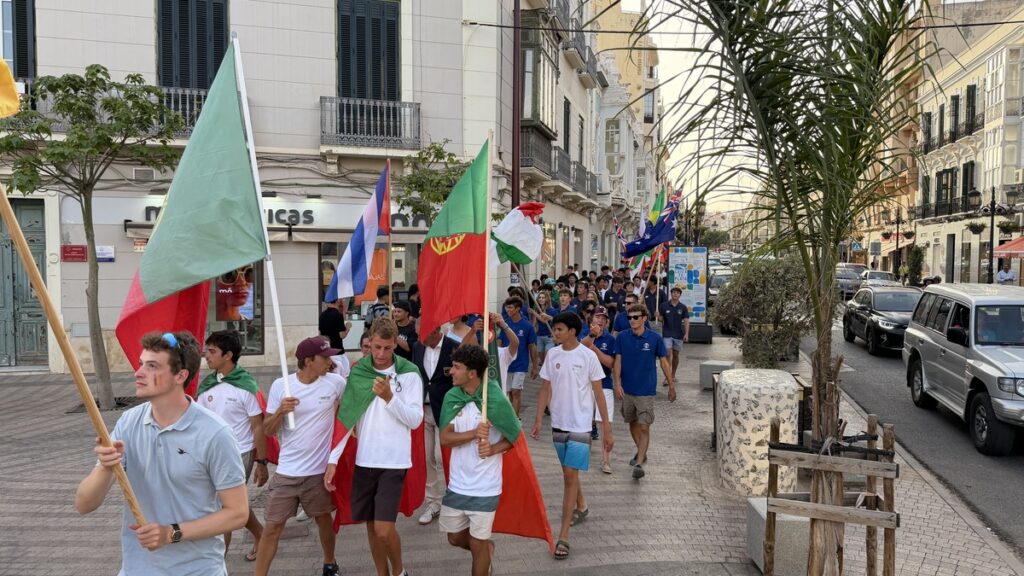 Group of young people marching down a city street, carrying large national flags (Italy, Portugal) during a parade.