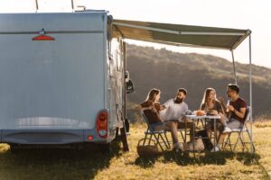 Grupo de amigos disfrutando de una comida al aire libre junto a una caravana