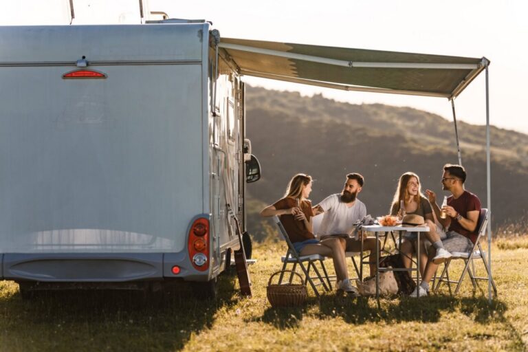 Grupo de amigos disfrutando de una comida al aire libre junto a una caravana