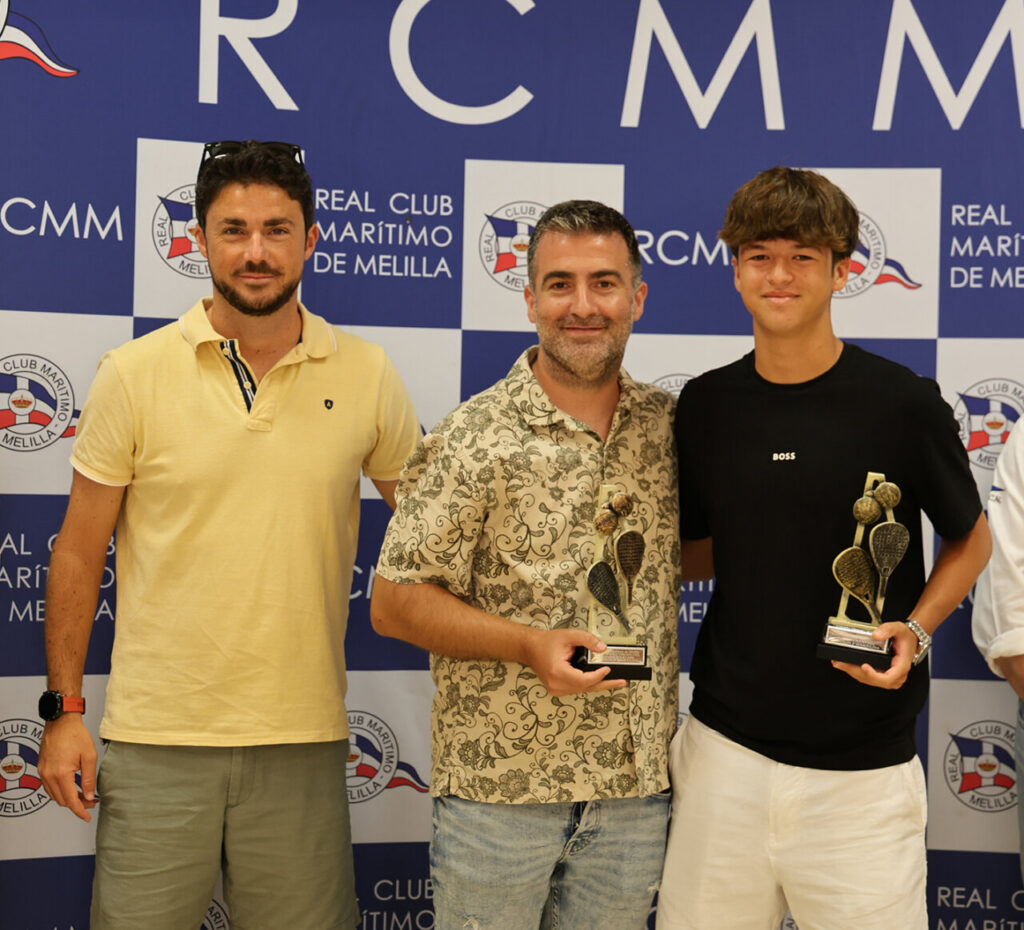 Three men stand together posing for a photo at an awards event, two holding trophies, against a blue sponsor backdrop.
