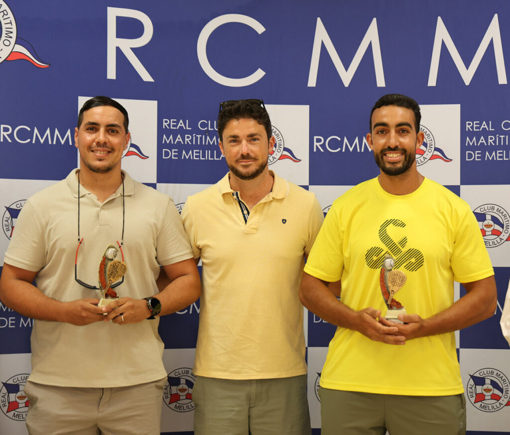 Three men standing side by side, two of them holding small trophies, in front of a blue RCMM event backdrop.