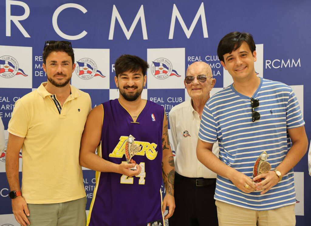 Four men pose with trophies at a Real Club event; one wears a Lakers jersey (#24), another in a striped shirt, against a RCMM backdrop.