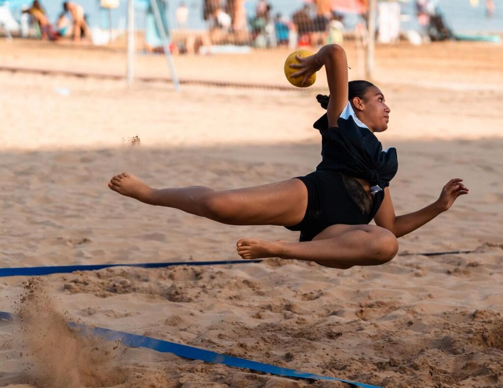 Jugadora de balonmano playa lanzando el balón en la arena.