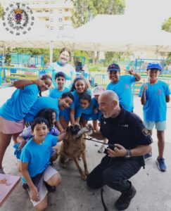 Grupo de niños con camisetas azules y un perro con un policía local.