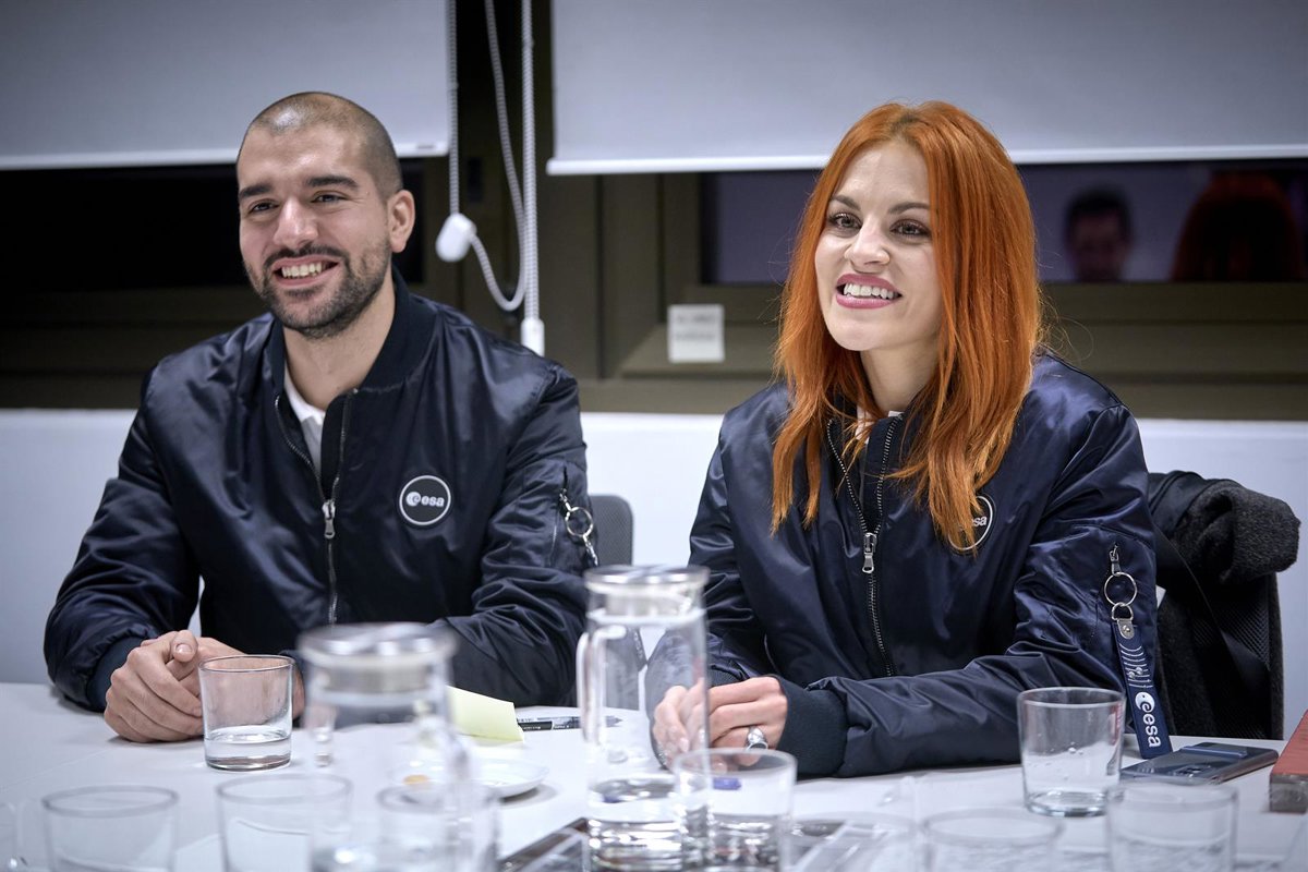 Two smiling colleagues in navy jackets with the Oesa logo sit at a conference table with glasses and a pitcher in front of them.