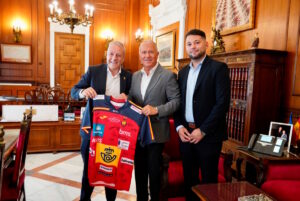 Tres hombres sosteniendo una camiseta de balonmano en un despacho