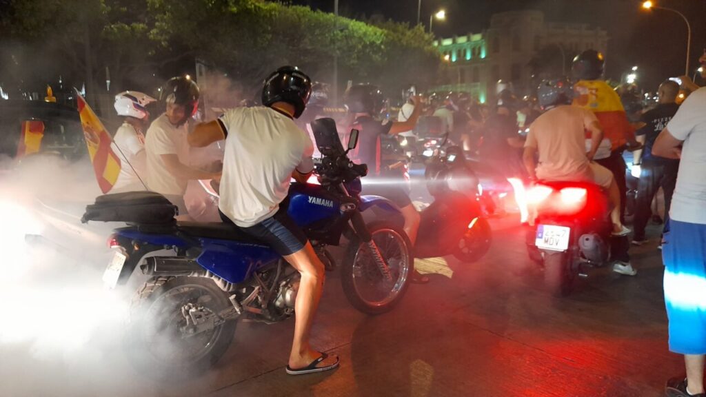 Night scene of a crowded street with motorbikes and riders, smoke in the air, and a blue Yamaha motorcycle in the foreground/s center.