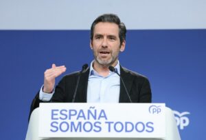Speaker at a podium delivering a political speech; banner reads 'ESPAÑA SOMOS TODOS' with PP logo in the background.