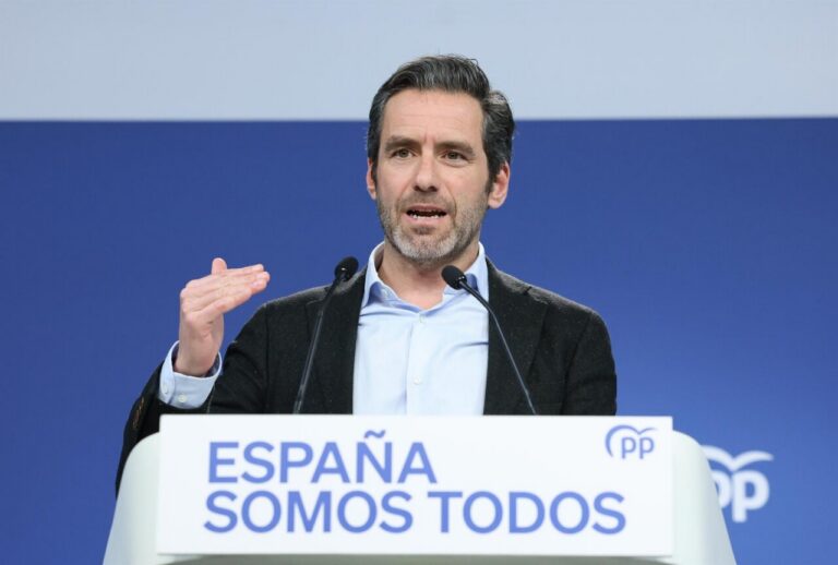 Speaker at a podium delivering a political speech; banner reads 'ESPAÑA SOMOS TODOS' with PP logo in the background.