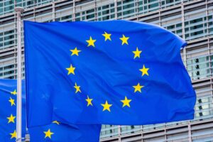 Blue European Union flag with yellow stars waving in wind against a modern glass building in the background