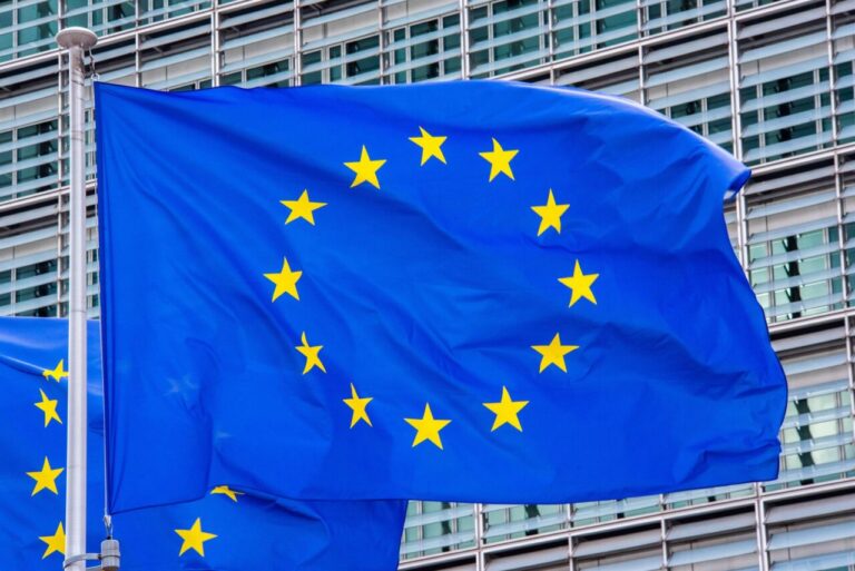 Blue European Union flag with yellow stars waving in wind against a modern glass building in the background
