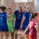 Group of women beach soccer players in blue celebrate together on a sandy field.