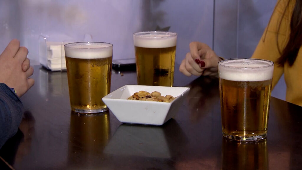Tres vasos de cerveza sobre una mesa con un plato de snacks