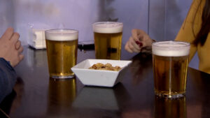 Tres vasos de cerveza sobre una mesa con un plato de snacks