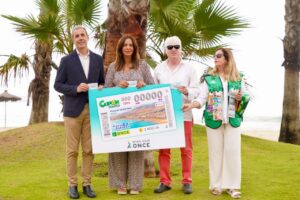 Group of four adults holding a large prize voucher at a beachfront park with palm trees in the background, smiling for the photo.