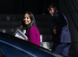 Mujer sonriendo con documentos en la mano frente a un edificio