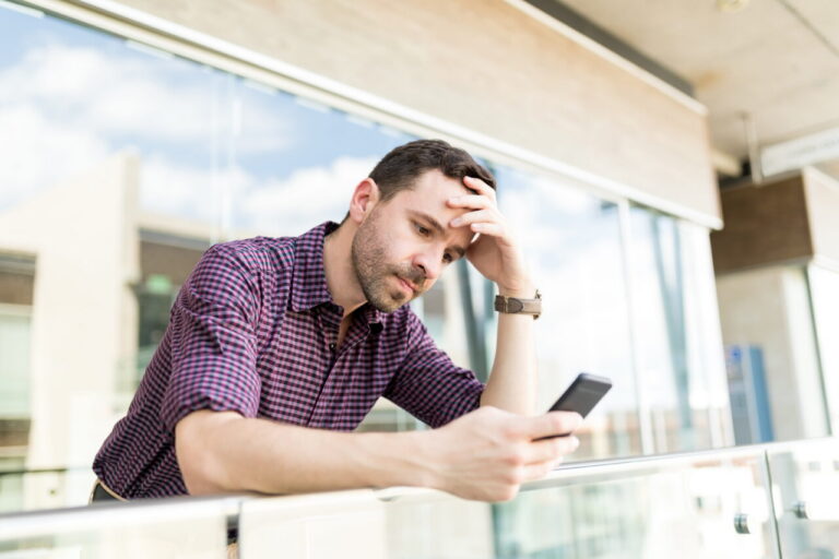 Hombre preocupado revisando su teléfono móvil en un balcón