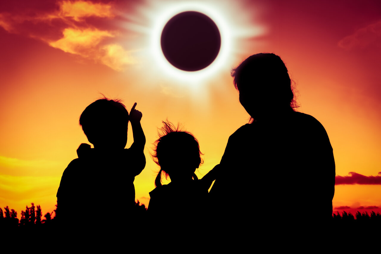 Silhouettes de niños y adultos observando un eclipse solar