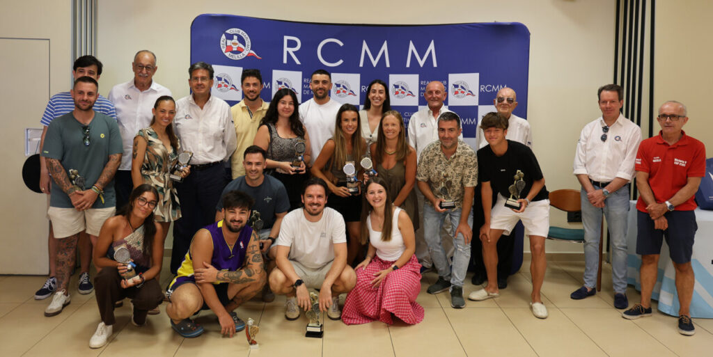 Group of people posing with trophies at an RCMM awards event in front of a blue backdrop
