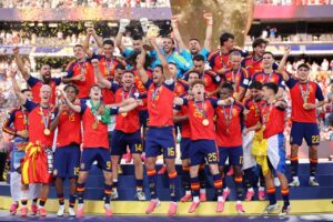 Spain national football team celebrating on a podium with the trophy and gold medals amid confetti, posing triumphantly as champions