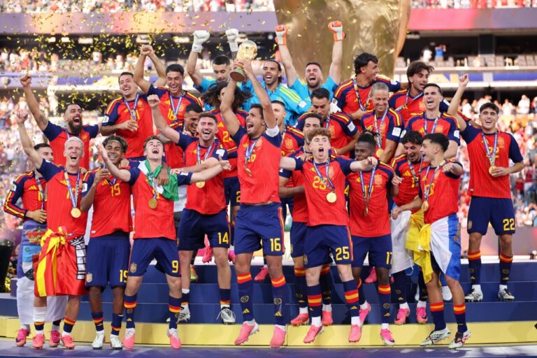 Spain national football team celebrating on a podium with the trophy and gold medals amid confetti, posing triumphantly as champions