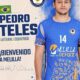 Male handball player in a blue jersey with the number 14, standing beside a welcome banner that says 'Bienvenido a Melilla' with the Melilla sports logo.