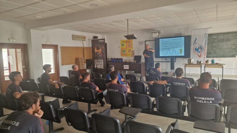 Firefighter training session in a classroom: instructor presenting slides to uniformed recruits wearing 'BOMBEROS MELILLA' shirts.