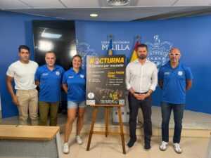 Five people stand in a row beside a poster promoting the Nocturna mountain race in a room with a blue backdrop and municipal insignia.
