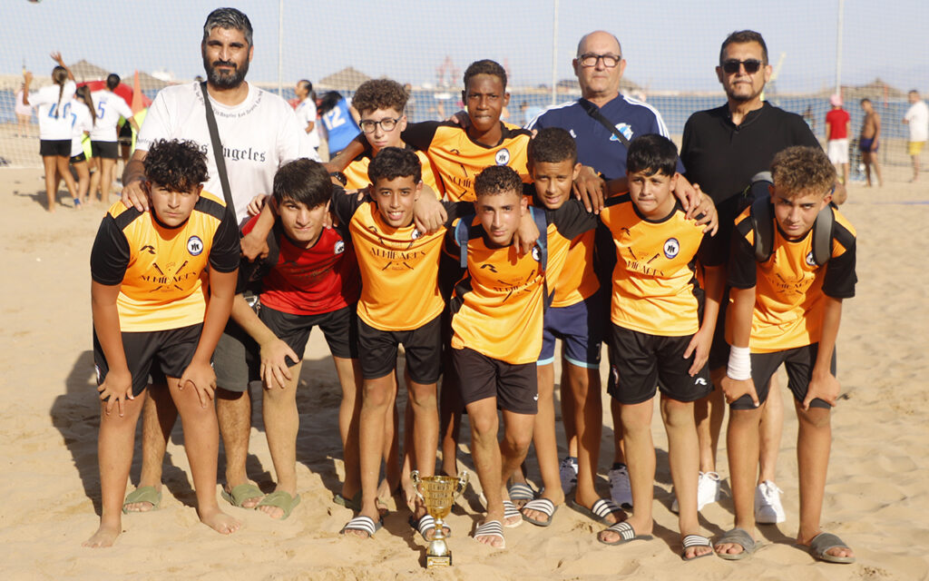 Equipo de fútbol infantil con trofeo en la playa de San Lorenzo