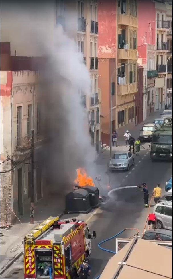 Incendio de contenedores en la calle Castelar de Melilla con bomberos apagando el fuego.