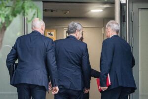 Grupo de hombres de espaldas saliendo de un edificio judicial