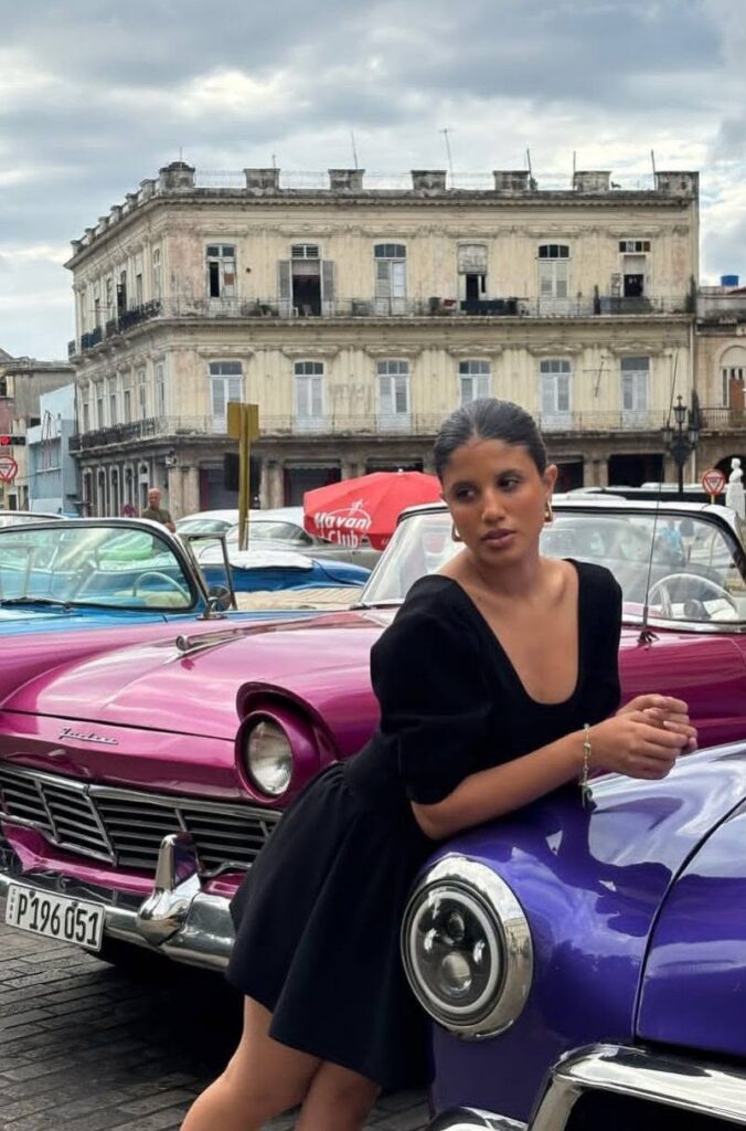 Melanie Santiler posando junto a coches clásicos de colores vibrantes