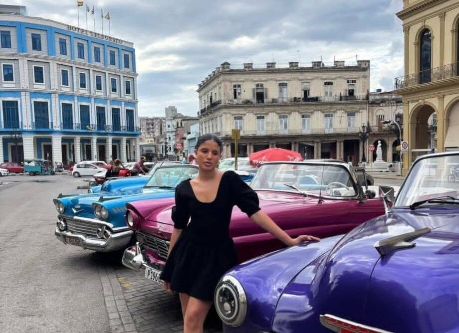 Melanie Santiler posando junto a coches clásicos en Cuba