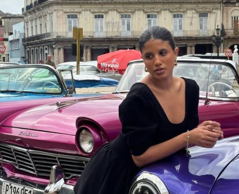 Melanie Santiler posando junto a coches clásicos de colores vibrantes