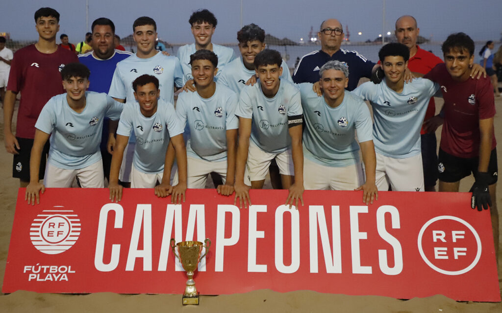 Youth soccer team posing on a beach with a red 'CAMPIONES' banner and a trophy in front.