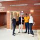 Group of four men standing and talking in a wood-paneled municipal lobby marked 'Tanatorio Municipal' near a doorway labeled Sala 3.