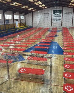 Indoor sports hall with many red portable bleachers arranged in neat rows, blue court markings, and protective netting in the foreground.