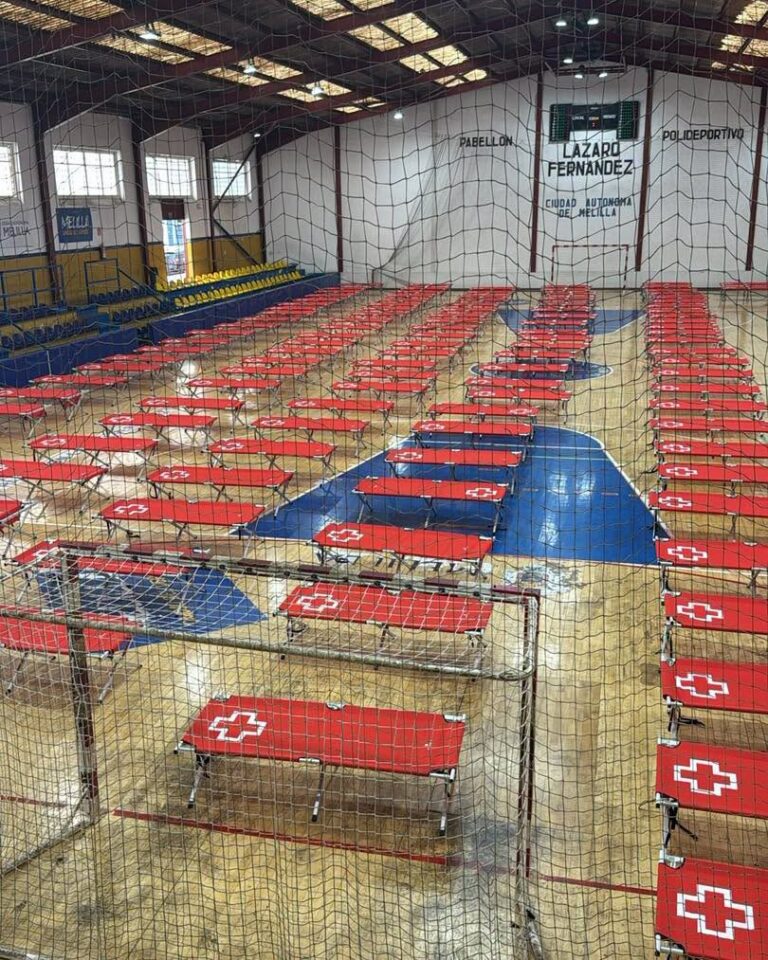 Indoor sports hall with many red portable bleachers arranged in neat rows, blue court markings, and protective netting in the foreground.