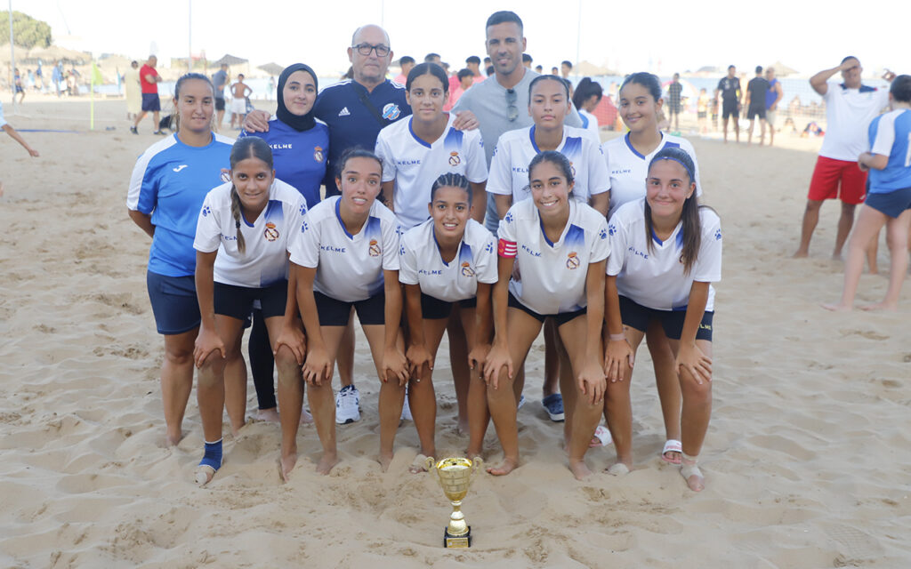 Equipo juvenil femenino de la Peña Real Madrid con trofeo en la playa